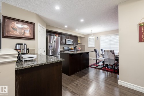 Kitchen and dining area featuring dark wood-finish cabinetry, stainless steel appliances, granite countertops, and wood-finish flooring - 59 655 Tamarack Road, Edmonton, AB 