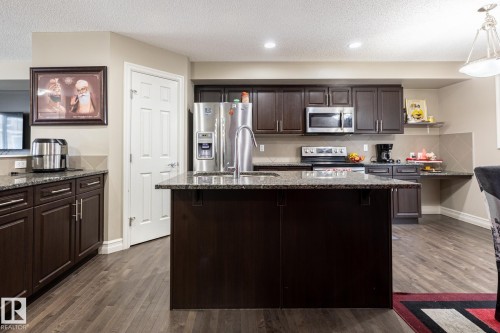 Kitchen featuring dark wood-finish cabinetry, stone countertops, stainless steel appliances, and wood-finish flooring - 59 655 Tamarack Road, Edmonton, AB 