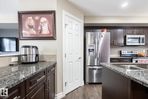 Kitchen featuring dark wood-finish cabinetry, granite countertops, and stainless steel appliances - 59 655 Tamarack Road, Edmonton, AB 