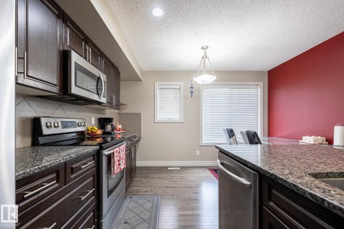 Kitchen featuring dark wood cabinetry, stainless steel appliances, granite countertops, and wood-finish flooring - 59 655 Tamarack Road, Edmonton, AB 