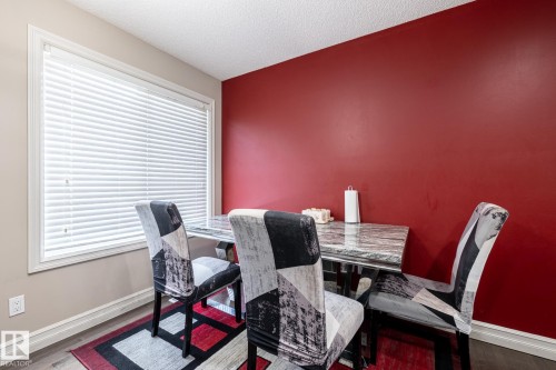 Dining area featuring a full-length window with white blinds, rich red accent wall, and wood-finish flooring - 59 655 Tamarack Road, Edmonton, AB 