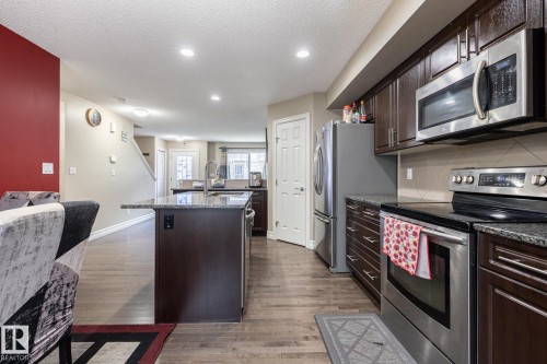 Kitchen featuring wood-finish flooring, dark wood cabinetry, stainless steel appliances, a center island with a stone-finish countertop, and recessed lighting - 59 655 Tamarack Road, Edmonton, AB 