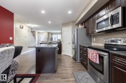 Kitchen featuring wood-finish flooring, dark wood cabinetry, stainless steel appliances, a center island with a stone-finish countertop, and recessed lighting - 
