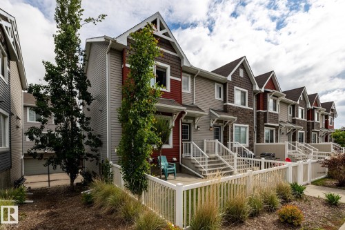Contemporary multi-level townhome featuring a gabled roofline, mixed siding facade, white exterior railings, and a fenced patio area - 59 655 Tamarack Road, Edmonton, AB 