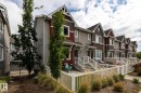 Contemporary multi-level townhome featuring a gabled roofline, mixed siding facade, white exterior railings, and a fenced patio area - 59 655 Tamarack Road, Edmonton, AB 