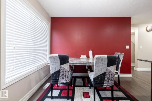 Dining area featuring a prominent red accent wall, a large window with white blinds, and wood-finish flooring - 59 655 Tamarack Road, Edmonton, AB 