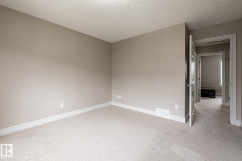 Neutral-toned room featuring light-colored carpet flooring, white baseboards, and a textured ceiling - 59 655 Tamarack Road, Edmonton, AB 