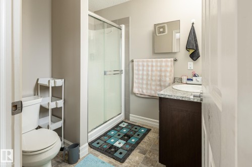 Three-quarter bathroom featuring a glass-enclosed shower, a white toilet, and a vanity with a granite-finish countertop and an integrated sink - 59 655 Tamarack Road, Edmonton, AB 
