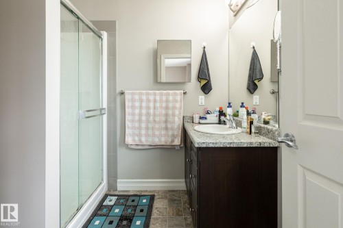 Bathroom featuring a glass-enclosed shower, a dark wood-finish vanity with an integrated sink, a light speckled countertop, and a large mirror - 59 655 Tamarack Road, Edmonton, AB 