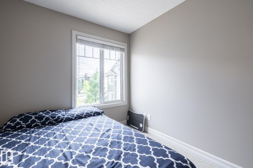 Bedroom featuring a large window with white trim, light gray painted walls, and textured carpet flooring - 59 655 Tamarack Road, Edmonton, AB 