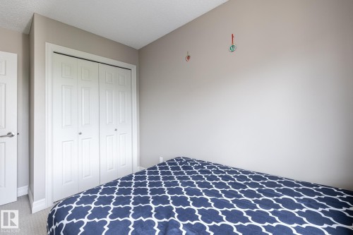 Neutral-toned bedroom featuring white bi-fold closet doors, textured ceiling, and light-colored carpeting - 59 655 Tamarack Road, Edmonton, AB 