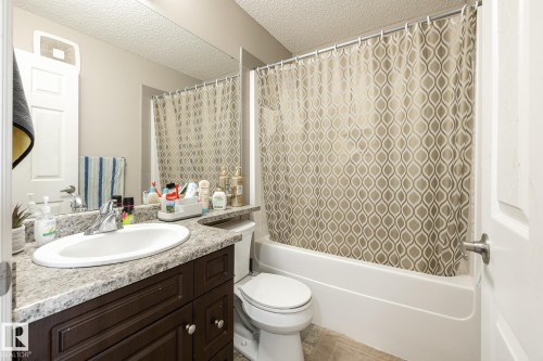 Bathroom featuring a dark wood-finish vanity with a single basin sink, speckle-patterned countertop, and an integrated shower-tub combination - 59 655 Tamarack Road, Edmonton, AB 