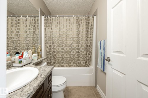 Full bathroom featuring a rectangular drop-in sink, stone-look countertop, dark wood-finish vanity, and a tub/shower combination - 59 655 Tamarack Road, Edmonton, AB 