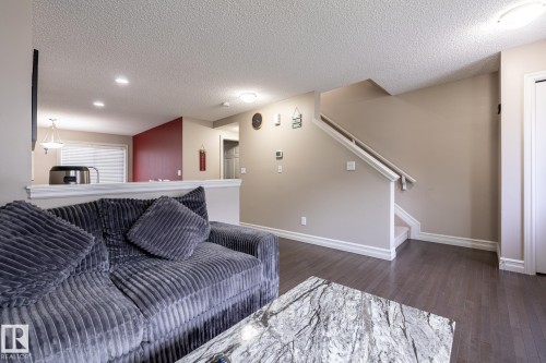 Open concept living space featuring wood-finish flooring, a neutral color palette, recessed lighting, a half-wall partition, and a staircase with a white railing - 59 655 Tamarack Road, Edmonton, AB 