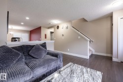 Open concept living space featuring wood-finish flooring, a neutral color palette, recessed lighting, a half-wall partition, and a staircase with a white railing - 