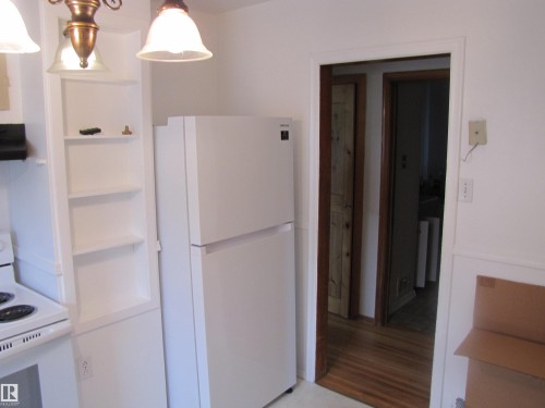 Kitchen space featuring a white refrigerator and electric range, integrated shelving, and a chandelier-style light fixture - 8122 83 Avenue, Edmonton, AB 