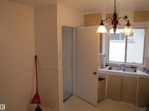 Kitchen area featuring a double-basin stainless steel sink, a window with frosted lower panes, wood-finish base cabinetry, and a three-light chandelier - 8122 83 Avenue, Edmonton, AB 