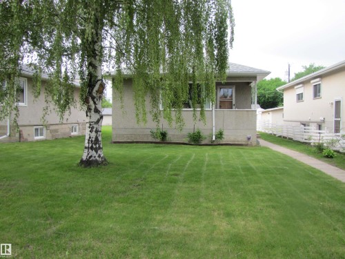 Stucco exterior with a covered front porch, an established front lawn, a mature birch tree, and a concrete walkway - 8122 83 Avenue, Edmonton, AB 