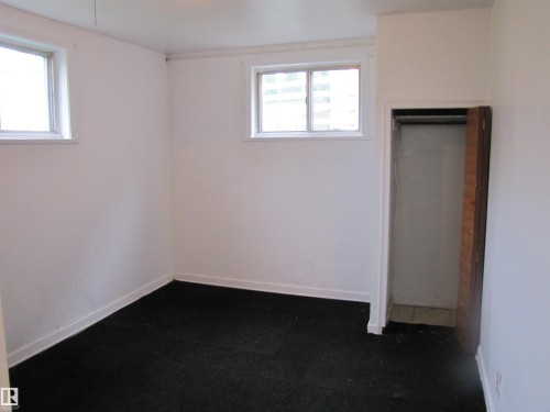 White-painted room featuring two windows, dark-colored carpeting, white baseboards, and a built-in closet with an open wooden door - 8122 83 Avenue, Edmonton, AB 
