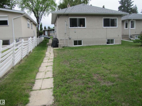 Rear exterior featuring a stucco finish, multiple windows, and a gray shingle roof - 8122 83 Avenue, Edmonton, AB 