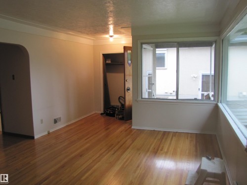 Hardwood flooring, coved ceilings, and crown molding define this room, featuring an arched doorway and a corner window arrangement - 8122 83 Avenue, Edmonton, AB 