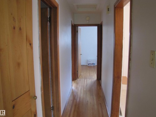 Hallway featuring wood-finish flooring, light-toned wall paint, and natural wood doors with corresponding trim - 8122 83 Avenue, Edmonton, AB 