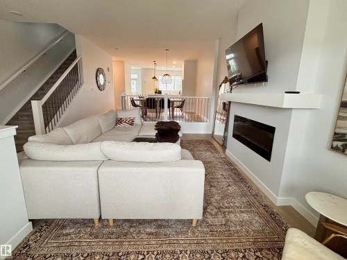 Open-concept living space featuring wood-finish flooring, a contemporary fireplace with a white mantel, and a staircase with dark metal spindles - 5281 Edgemont Boulevard, Edmonton, AB 