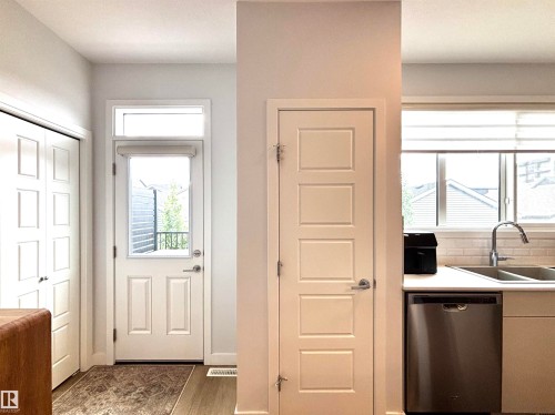Entrance area with wood-finish flooring, a white paneled door with an overhead transom window, and a built-in closet with bi-fold doors - 5281 Edgemont Boulevard, Edmonton, AB 