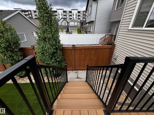 Composite deck stairs with black metal railings descending to a yard featuring artificial turf and decorative gravel - 5281 Edgemont Boulevard, Edmonton, AB 