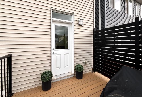 Exterior patio featuring wood-finish decking, horizontal slat privacy fencing, and a modern wall sconce - 5281 Edgemont Boulevard, Edmonton, AB 