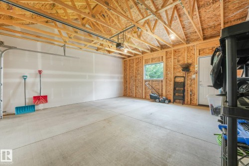 Spacious garage featuring a concrete floor, exposed wood ceiling trusses, and a side window - 5281 Edgemont Boulevard Nw, Edmonton, AB - Indoor Photo Showing Garage