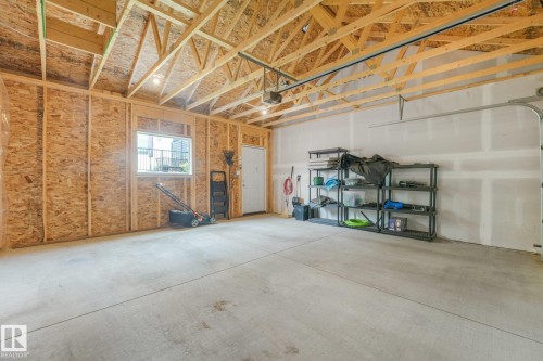 Spacious garage featuring a concrete floor, exposed wood framing, an overhead door mechanism, a white interior door, and a window - 5281 Edgemont Boulevard Nw, Edmonton, AB - Indoor Photo Showing Garage