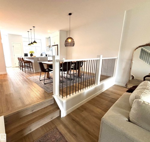 Open-concept interior featuring wood-finish flooring, a white railing with black metal balusters, and a contemporary pendant light fixture - 5281 Edgemont Boulevard, Edmonton, AB 