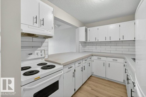 Kitchen featuring light wood-finish flooring, white cabinetry with black hardware, white subway tile backsplash, light-toned countertops, and a white electric range - 103 10620 104 Street Nw, Edmonton, AB 