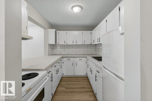 Galley kitchen featuring white cabinetry with black hardware, light-toned countertops, subway tile backsplash, wood-finish flooring, and a white electric range - 103 10620 104 Street Nw, Edmonton, AB 