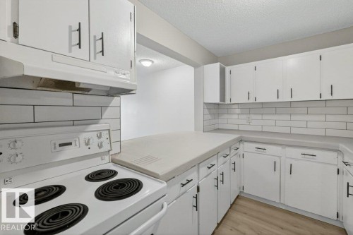 Bright kitchen featuring white cabinetry, black hardware, subway tile backsplash, light countertops, and wood-finish flooring - 103 10620 104 Street Nw, Edmonton, AB 