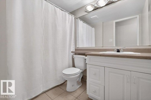 Bathroom featuring a white vanity with paneling and chrome hardware, an integrated sink, and a large wall-mounted mirror - 103 10620 104 Street Nw, Edmonton, AB 