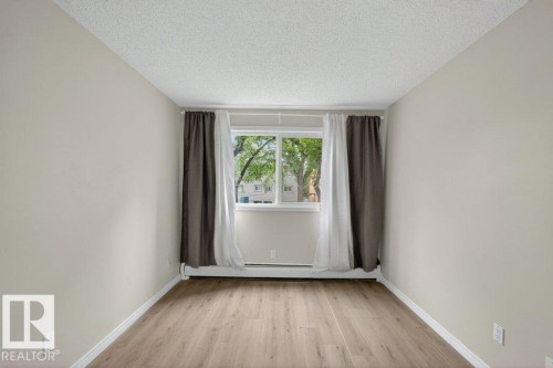 Bright room featuring neutral wall paint, wood-finish flooring, white baseboards, and a window with white trim - 103 10620 104 Street Nw, Edmonton, AB 