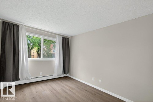 Room with wood-finish flooring, a large window, and light-colored walls - 103 10620 104 Street Nw, Edmonton, AB 