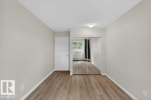 Neutral tone wall paint with white trim, wood-finish flooring, and mirrored closet doors - 103 10620 104 Street Nw, Edmonton, AB 