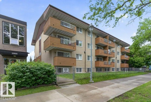 Multi-story building featuring individual balconies with brown wood-finish railings, a stucco exterior, and a flat roofline - 103 10620 104 Street Nw, Edmonton, AB 