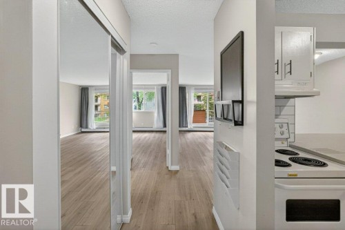 Open-concept living space with wood-finish flooring, light-toned walls, and multiple large windows - 103 10620 104 Street Nw, Edmonton, AB 