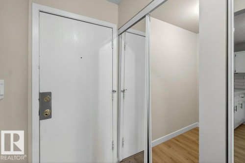 Entryway featuring a white door with brass hardware, light wood-finish flooring, and a mirrored closet door - 103 10620 104 Street Nw, Edmonton, AB 