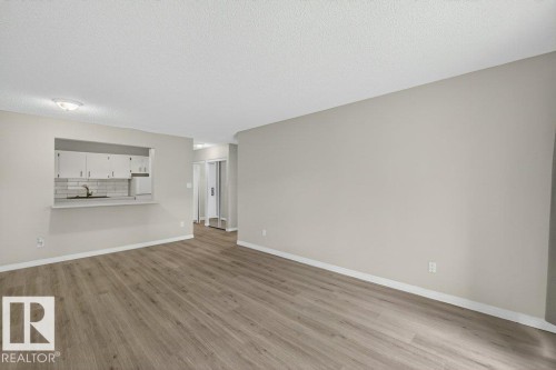 Open-concept living area featuring wood-finish flooring, a kitchen pass-through, shaker-style kitchen cabinetry, subway tile backsplash, and a contemporary ceiling light fixture - 103 10620 104 Street Nw, Edmonton, AB 