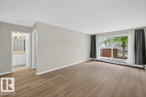 Spacious room featuring wood-finish flooring, light grey walls, and white trim - 103 10620 104 Street Nw, Edmonton, AB 