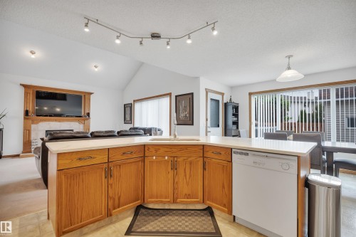 Open-concept kitchen featuring wood cabinetry, a built-in sink, and a dishwasher, with a vaulted ceiling and track lighting - 16512 87 Street, Edmonton, AB 