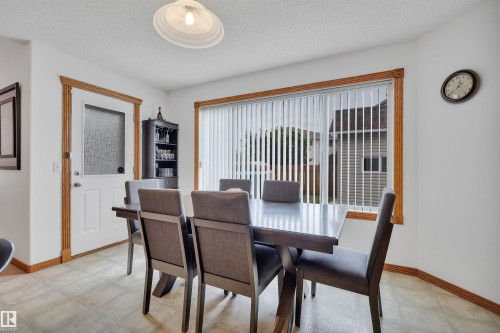 Dining area featuring a large window with vertical blinds, a white paneled door with frosted glass, wood-finish trim, and neutral-toned flooring - 16512 87 Street, Edmonton, AB 