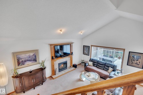 Vaulted ceiling living space featuring a wood-surround fireplace with a tiled hearth, an expansive window with vertical blinds, and neutral carpeting - 16512 87 Street, Edmonton, AB 