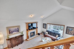 Vaulted ceiling living space featuring a wood-surround fireplace with a tiled hearth, an expansive window with vertical blinds, and neutral carpeting - 