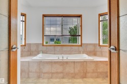 Built-in soaking tub with a tiled surround, three windows with wood-frame trim, and tile flooring - 